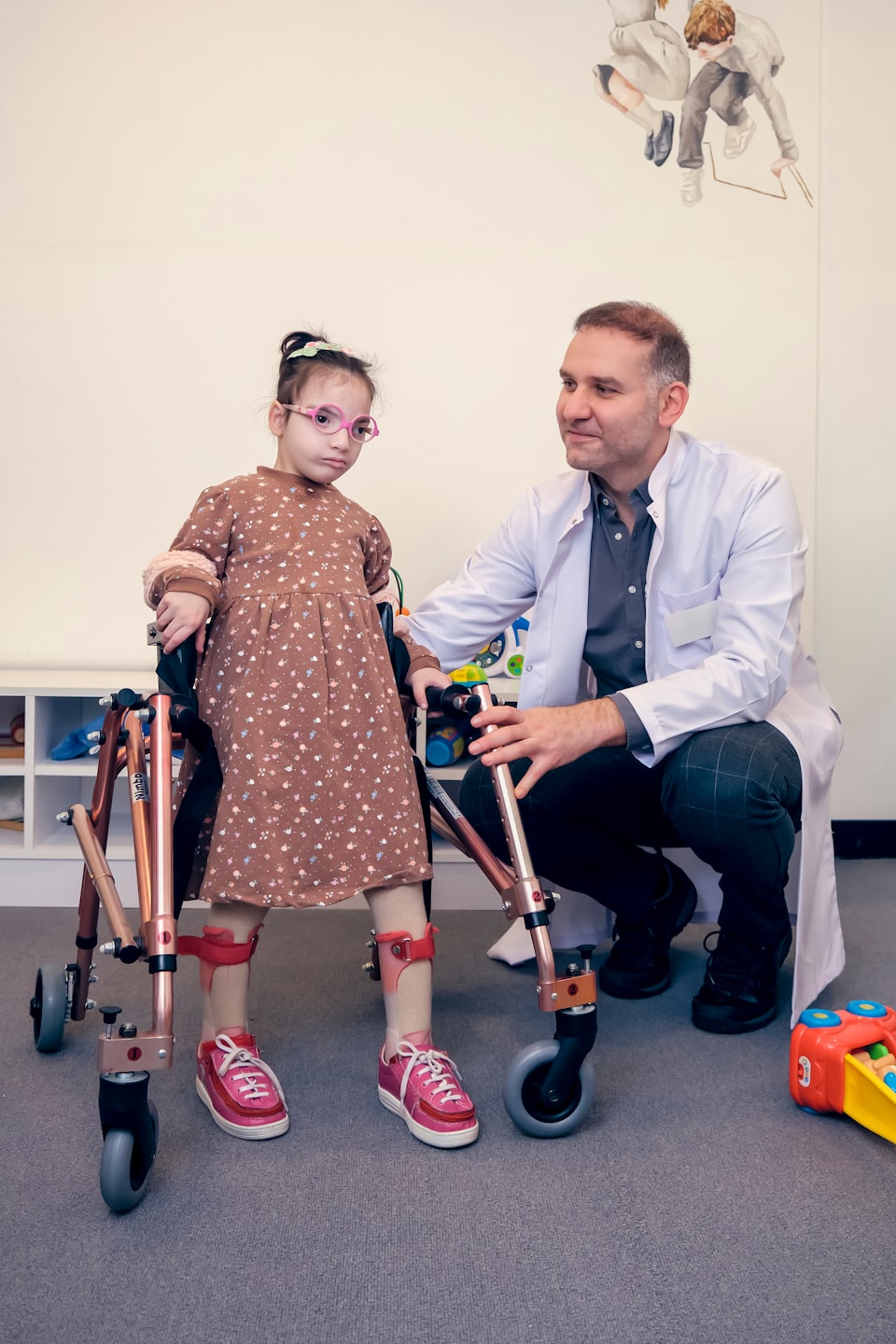 Doctora ayuda a una niña con aparatos en las piernas a usar un andador.